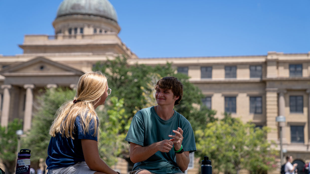 two students sitting in front of the academic building