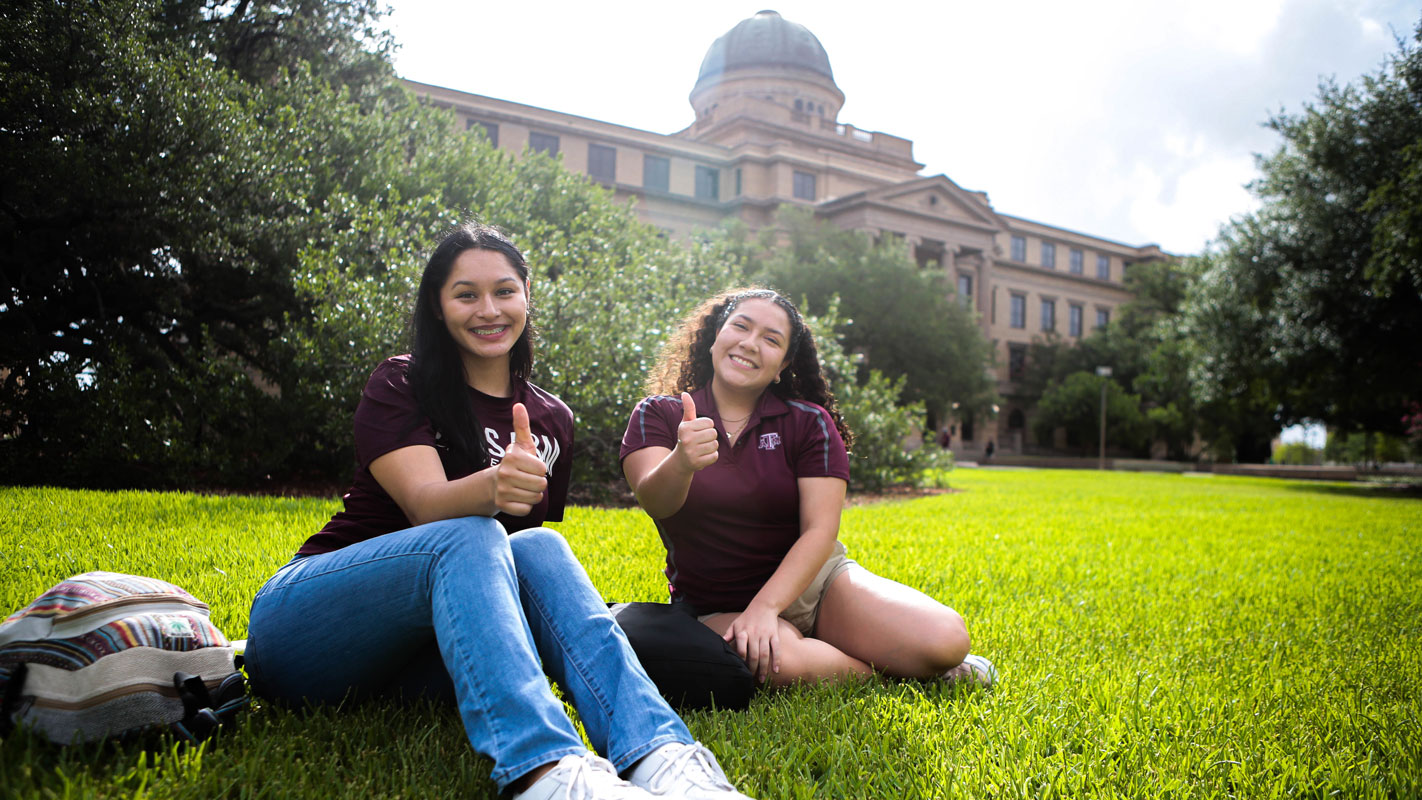 Students sitting in the grass in front of a building